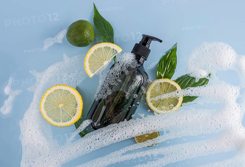 Luxurious black bottle of shower gel with lemon slices and green leaves, surrounded by frothy bubbles on a light blue background, exuding freshness and invigoration