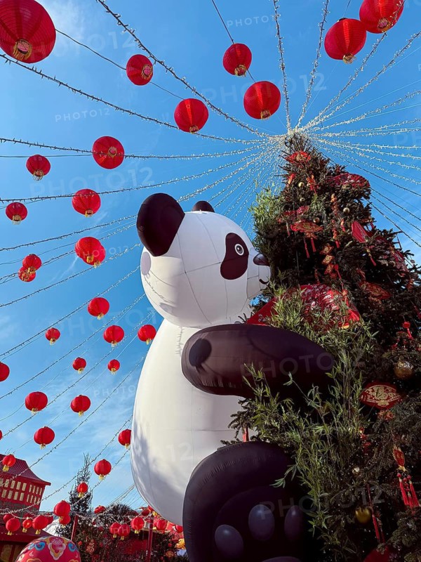 Vibrant Chinese New Year decorations adorn the streets, featuring bright red lanterns and a large inflatable panda, creating a festive and joyful atmosphere for all to enjoy