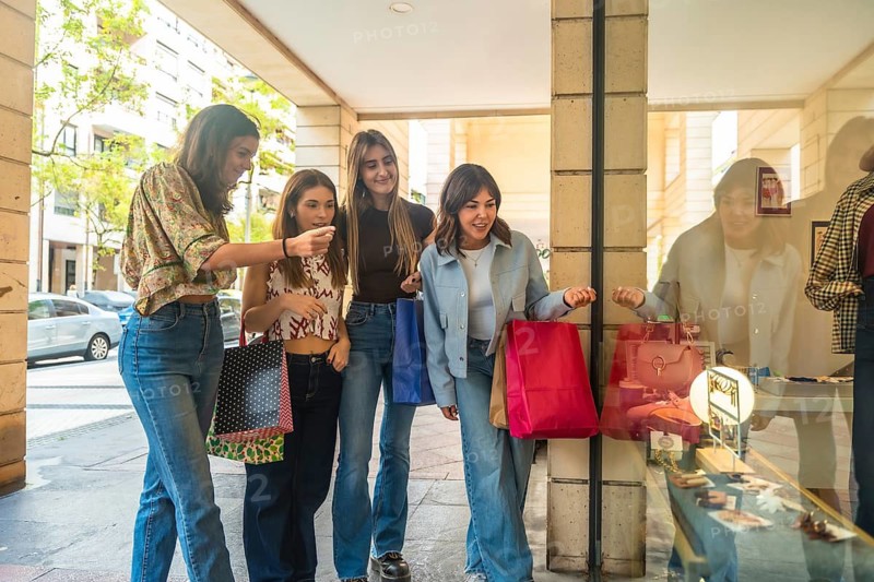 Young women enjoying a leisurely day out, walking along a shopping arcade, looking at displays, and carrying colorful bags filled with purchased items
