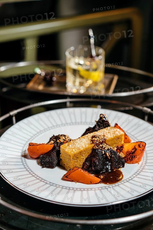 A gourmet dish featuring tender braised veal cheeks, served alongside creamy polenta. Perfectly garnished with vibrant vegetables for a luxurious dining experience