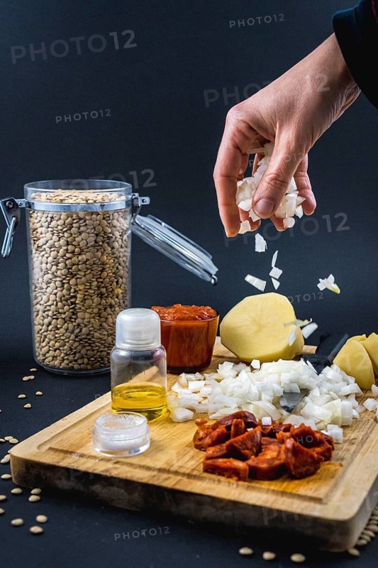 Adding onion with a woman's hand to the ingredients. Homemade recipe of a Spanish lentil dish