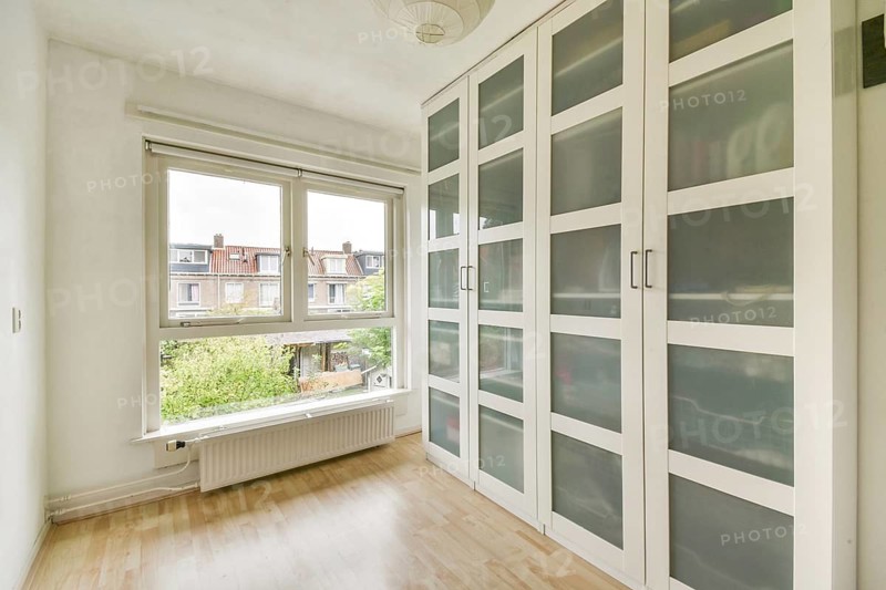A bright and airy room featuring large windows letting in natural light and a modern, white wardrobe with frosted glass doors, creating a spacious and elegant atmosphere