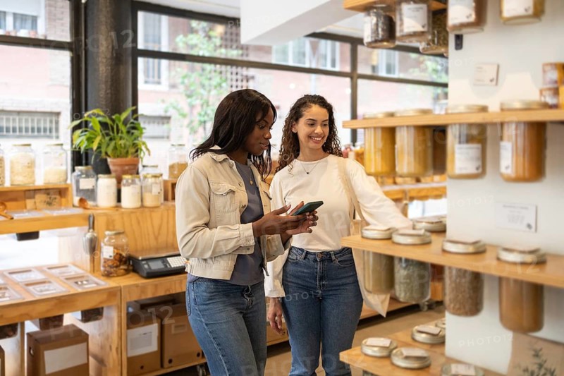 Two women explore the variety of products in an organic supermarket. They appear engaged and interested in healthy choices, reflecting a commitment to sustainable living