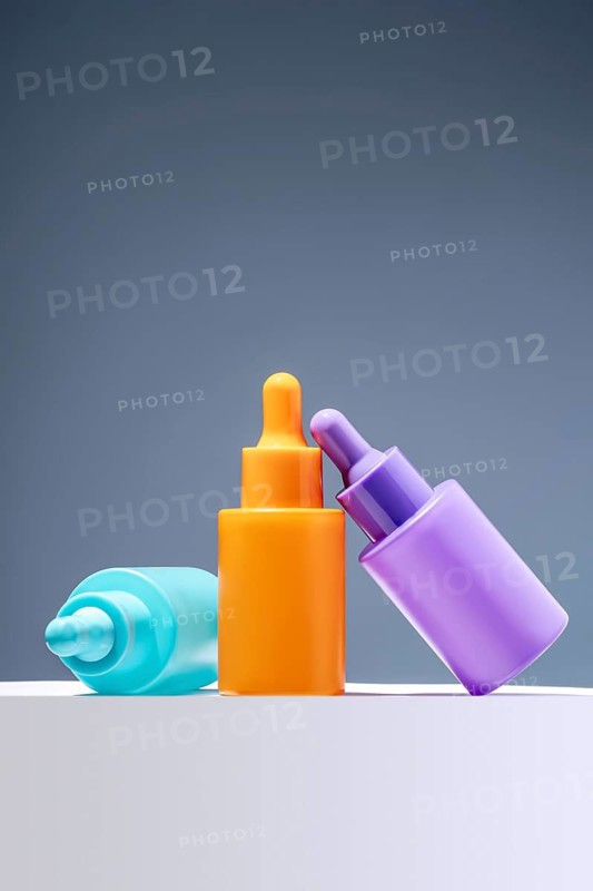 Three colorful serum bottles arranged against a plain gray background, highlighting vibrant shades of blue, orange, and purple