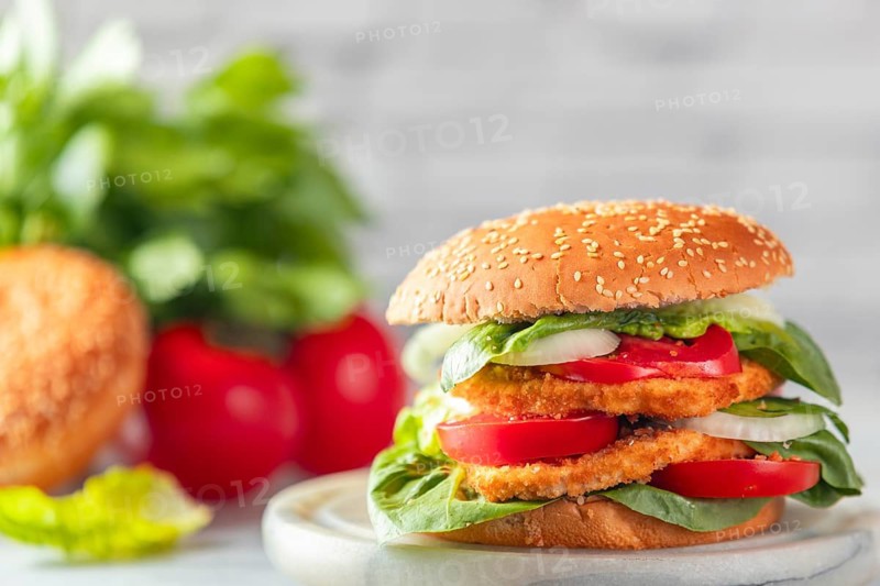 Burger with vegan schnitzel, tomatoes, onions and salad in bright surroundings with ingredients in the background