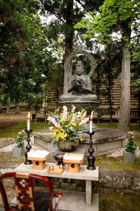 A peaceful Buddha statue surrounded by lush greenery and flowers at Ninna-ji temple in Kyoto, Japan, captures the essence of tranquility and spiritual reverence