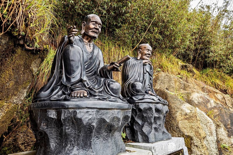Two meditating monk statues sit on stone platforms against a lightly wooded background, The Buddha statues at Fansipan near Sa Pa in Vietnam