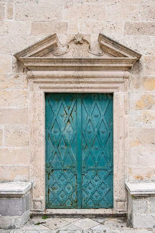 Antique green wooden door with elaborate decorations embedded in a stone wall, The island of Gospa od Skrpjela, Mary of the Rock, Bay of Kotor, Montenegro, Balkans