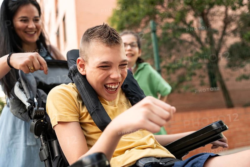 A mother joyfully spends time outdoors with her children, including a girl with a tracheostomy and a boy with cerebral palsy, highlighting love and inclusivity