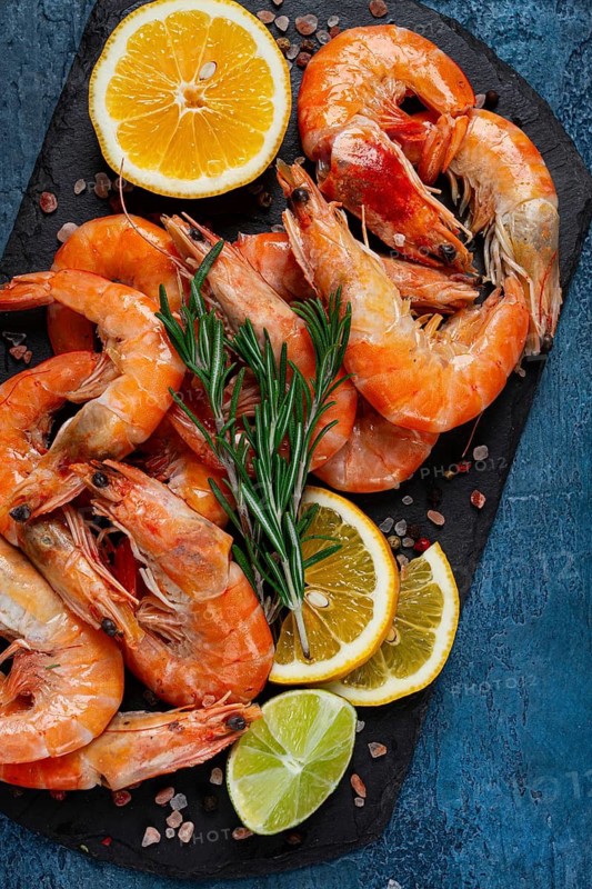 Freshly frozen shrimp, with lemon and rosemary, on black slate, close-up, top view, no people