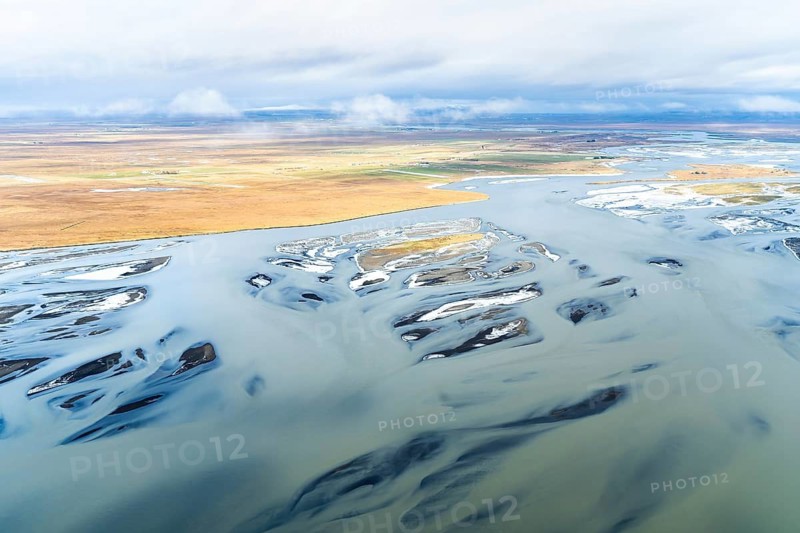 A stunning aerial shot capturing the dynamic rivers along Iceland's coast, showcasing swirling water patterns amid diverse terrain under a cloud-laden sky