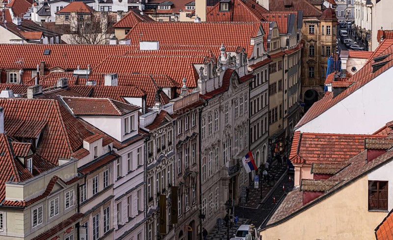 Scenic bird's-eye view of densely packed red rooftops in Prague's historic center, showcasing Baroque architecture and winding streets with pedestrians