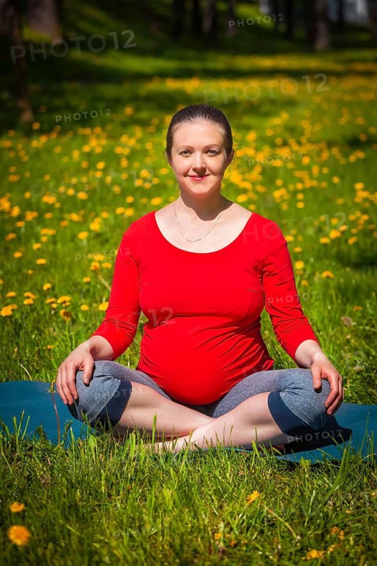 Pregnancy yoga exercise, pregnant woman doing asana Sukhasana easy yoga pose outdoors on grass lawn with dandelions in summer