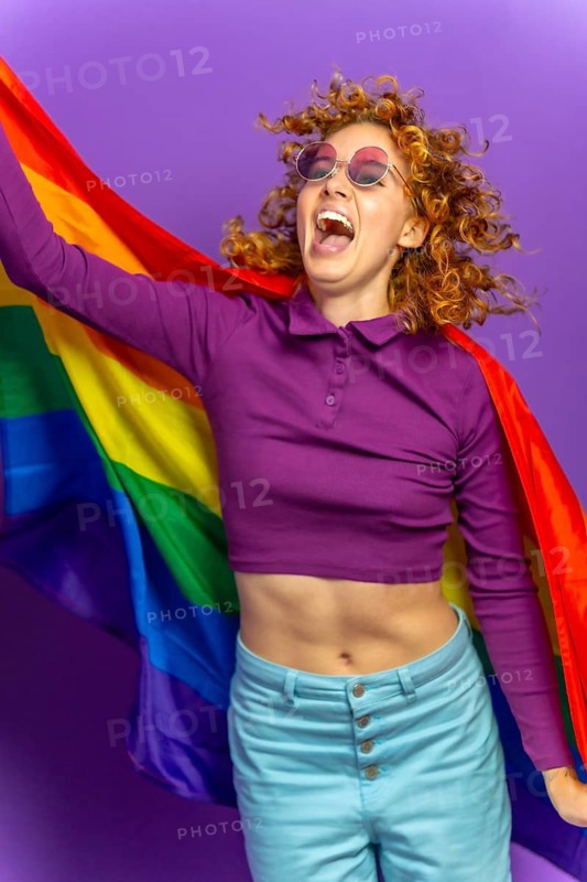 Studio portrait with purple background of a happy woman jumping holding lgbt rainbow flag