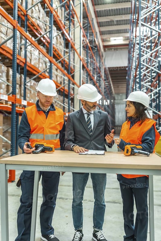 Warehouse workers and manager discussing logistics while using barcode scanners in a large distribution center