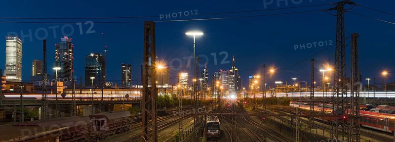View over rails and moving train to the main station, in the background the colourful skyline of Frankfurt am Main at blue hour, panorama, Gallusviertel, Frankfurt am Main, Hesse, Germany
