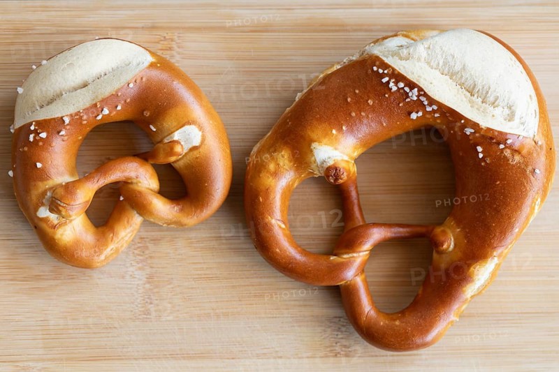 Two pretzels, one craft. Tradition served on a wooden board. A small and a normal pretzel from a traditional baker from Germany
