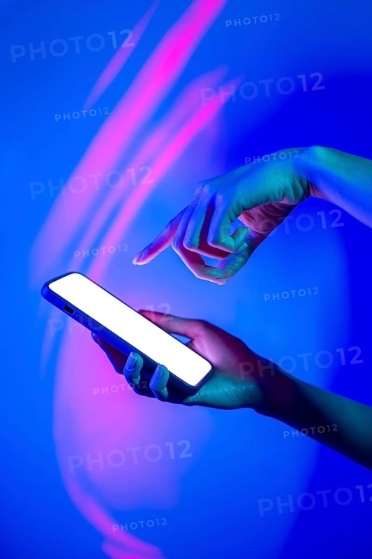 A hand interacts with a smartphone under vibrant neon lighting, highlighting the modern use of technology in a vividly colorful environment, creating a futuristic mood