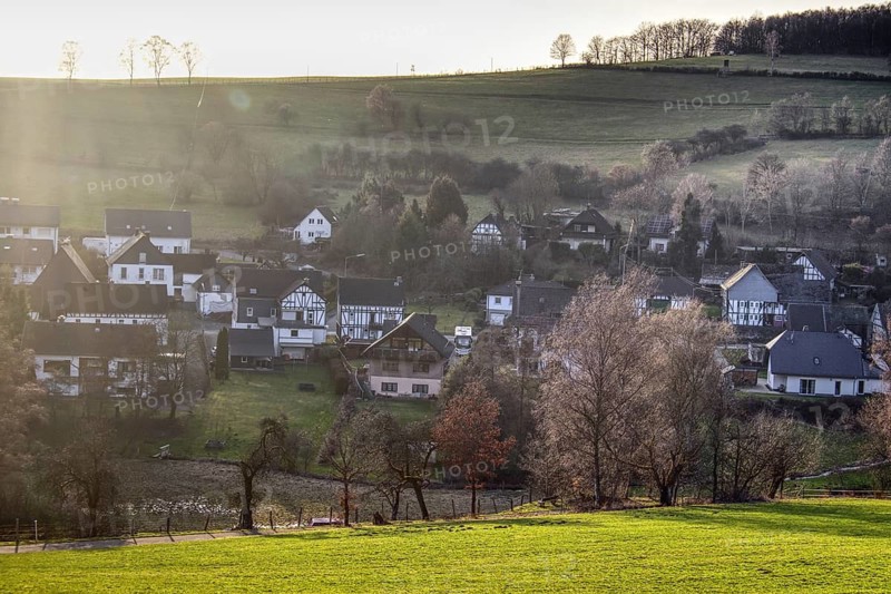Partial view of Langenholdinghausen with village character amidst green hills in warm sunlight with scattered trees, Siegen North Rhine-Westphalia