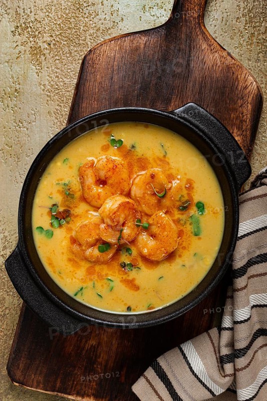 Creamy shrimp curry with spices, garnished with herbs, on a textured background, homemade, no people