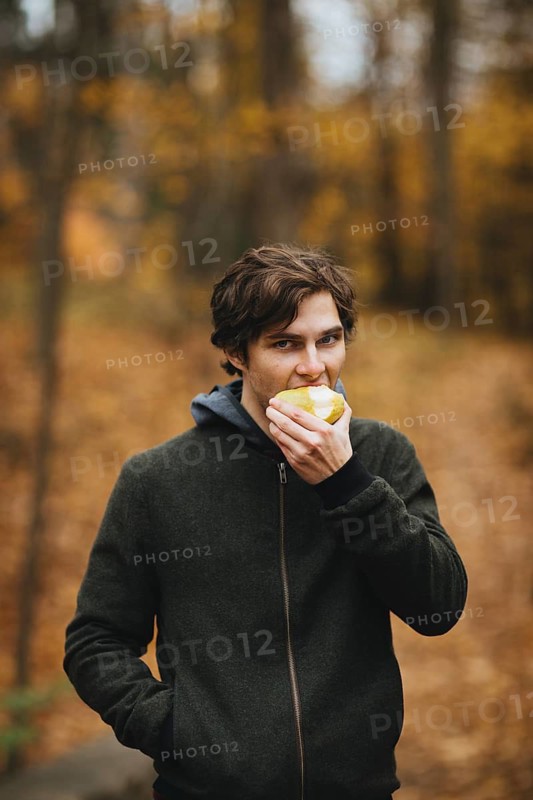 A man enjoys a fresh apple in a serene Quebec forest during autumn, surrounded by vibrant fall foliage. The crisp air and colorful leaves create a peaceful, natural setting
