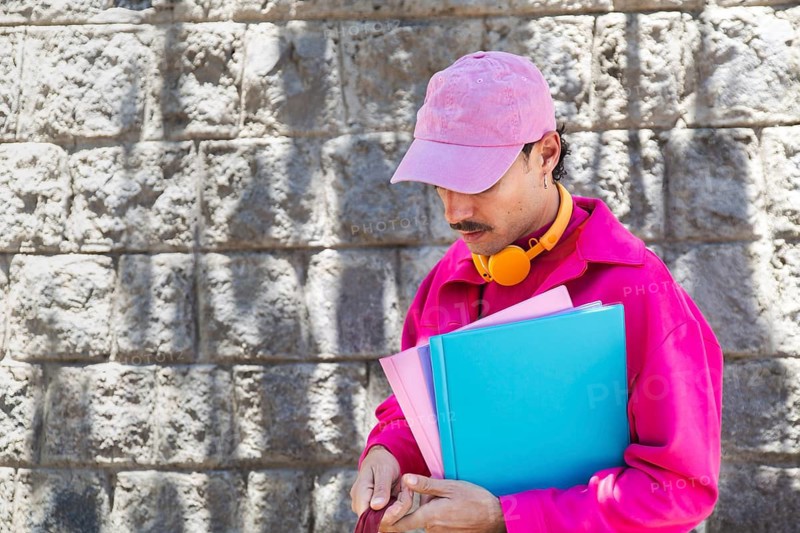 A Spanish LGTBIQ+ man with a mustache dressed in vibrant pink clothing holds folders and takes in the ambiance of Quito, Ecuador. Captured in a casual urban setting, he conveys a relaxed, cheerful lifestyle, embracing individuality and diversity