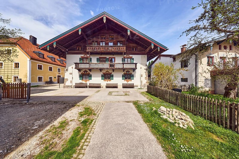 Town hall, alpine building, commercial building, balcony, façade with windows, shutters and ventilation painting, benches, general architecture, wooden fence, walkway, trees with spring leaves, lawn, blue sky, cumulus clouds, cirrostratus clouds, town hall square, Ruhpolding, district of Traunstein, Bavaria, Germany