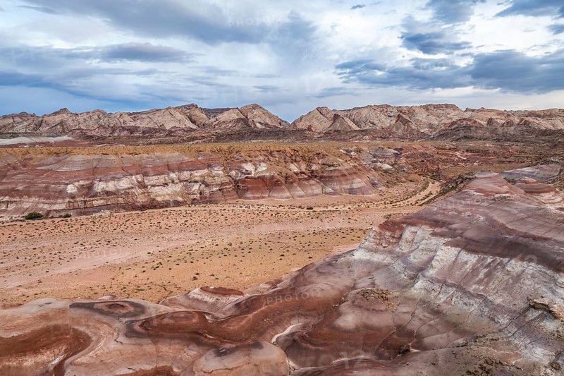 A striking aerial drone shot captures the diverse, rugged terrain of Hanksville, Utah, showcasing the area's colorful striated rock formations and vast desert expanses
