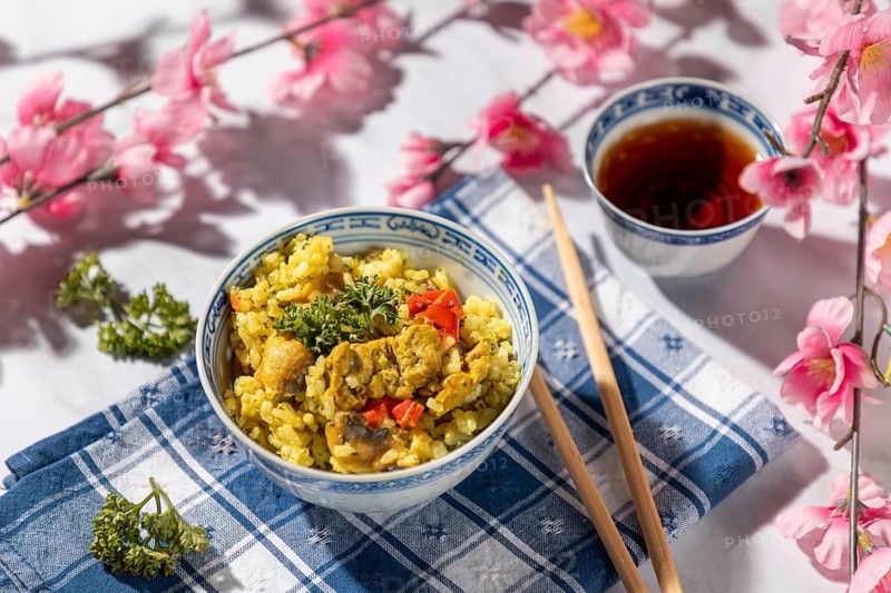 Chinese bowl with rice and vegetables next to tea, decorated with cherry blossoms