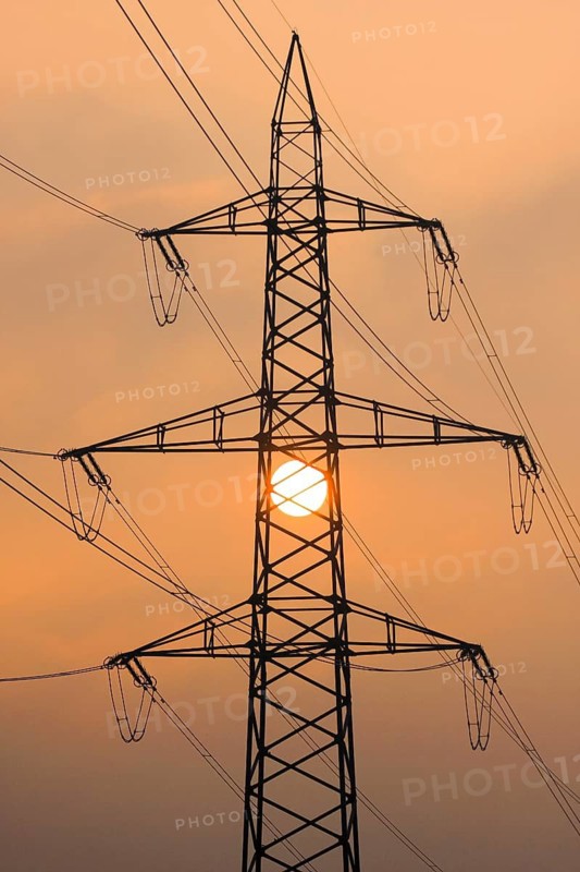 Setting sun behind silhouette of high-voltage power line pylons, shrouded in orange light amidst fog, Canton Zurich, Switzerland