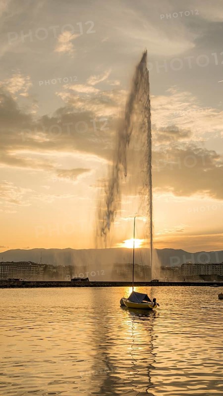 A serene evening scene capturing the iconic Jet d'Eau fountain and a solitary sailboat against the backdrop of a sunset in Geneva