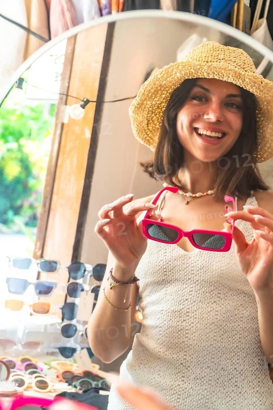 Happy tourist wearing straw hat trying on pink sunglasses in a souvenir shop in siargao island, philippines