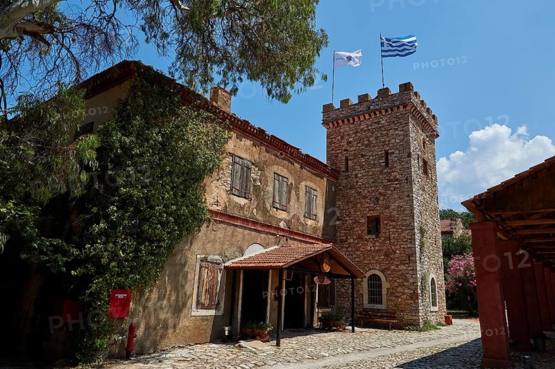 A historic building with a tower surrounded by trees and two flags, Achaia Clauss Winery, Patras, Peloponnese, Greece