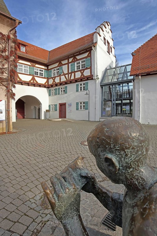 Historical town library with stepped gable and fountain with sculpture newspaper reader, Pfleghof, bronze sculpture newspaper, literature, book reader, reader, book, reading, head, figure, book, holding, hand, archway, Langenau, Alb-Donau district, Swabian Alb, Baden-Württemberg, Germany
