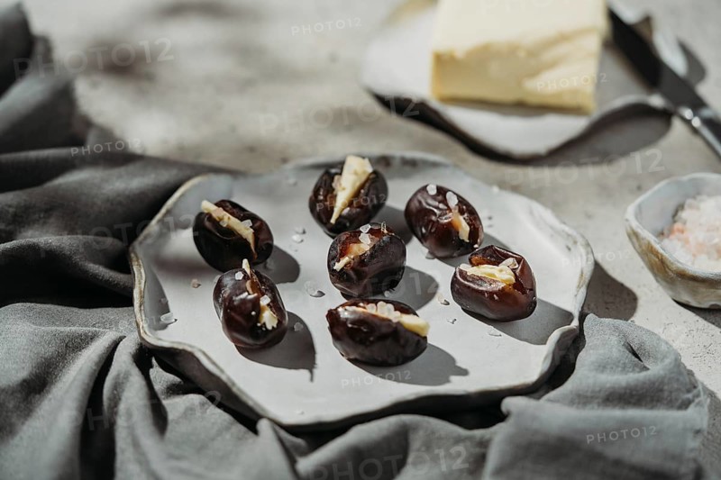 A plate of dates filled with creamy butter and sprinkled with sea salt. The rustic ceramic setting enhances the gourmet appeal, offering a delightful treat for the senses