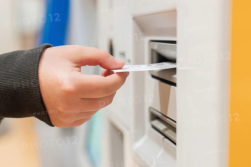 A passenger processes travel documents using an airport check-in kiosk. The close-up image highlights the hand placing a ticket. It conveys efficiency in modern air travel