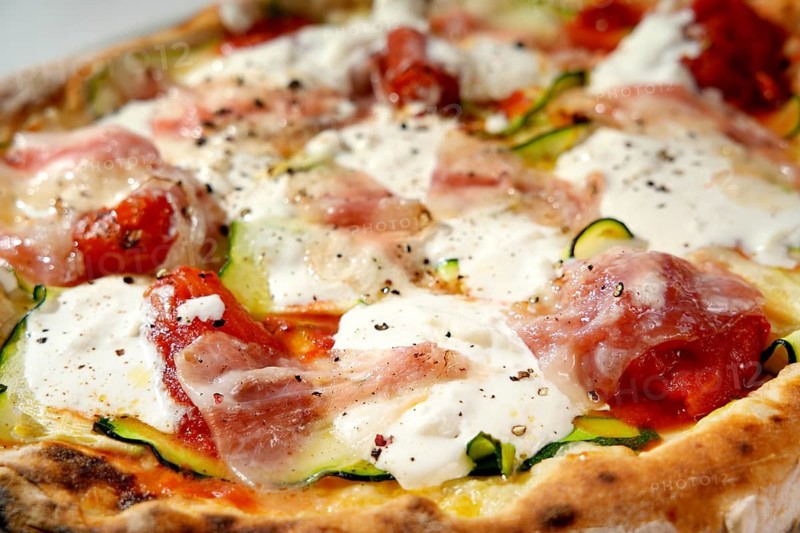 Detail shot of a delicious gourmet pizza with fresh toppings, including mozzarella, prosciutto, tomato, and zucchini on a perfectly baked crust