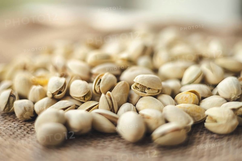 A close up image of shelled pistachios scattered on burlap, showcasing their natural texture. The soft focus background adds depth, highlighting the snack earthy tones