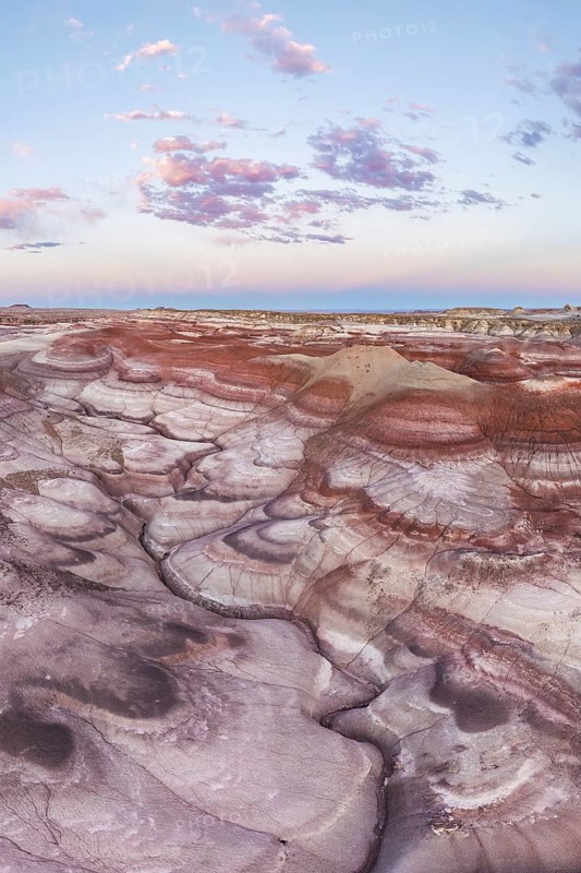 Captivating aerial image of the twisted and colorful bentonite hills in Utah, USA, under a sky dotted with soft pink clouds at sunset