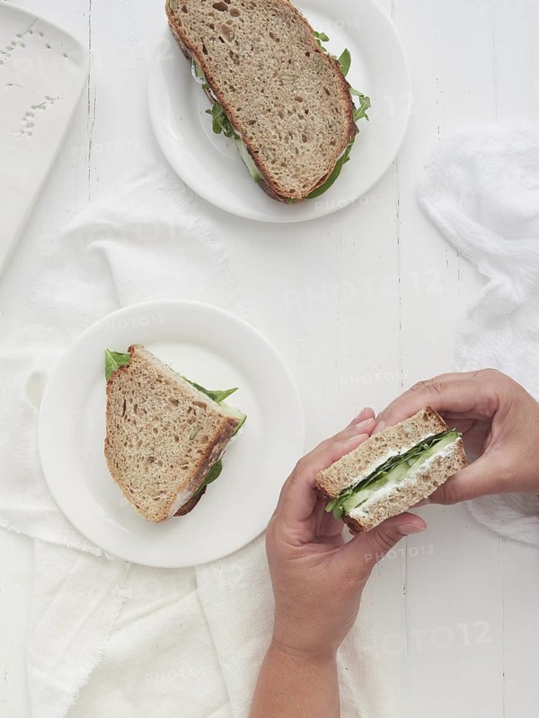 Hands holding half-cut vegetable sandwich of cucumber and spinach greens