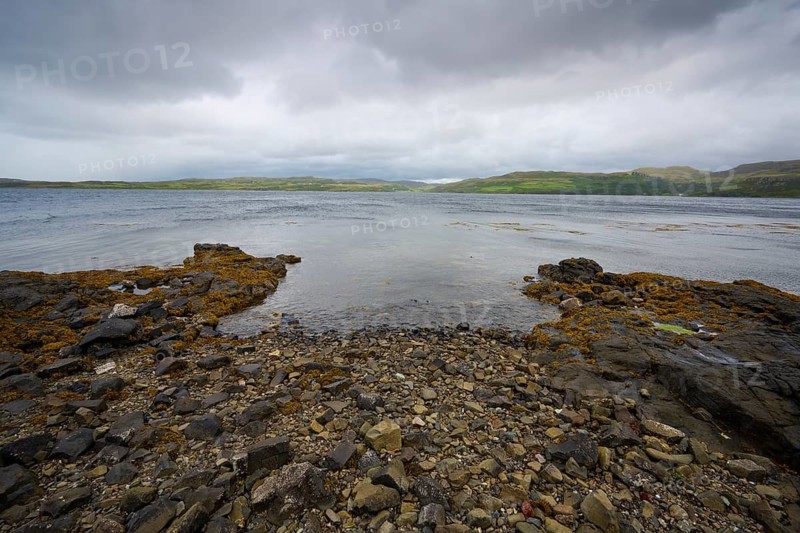 A rocky beach overlooking a murky lake under grey clouds, Portnalong, Isle of Skye, Scotland, United Kingdom, United Kingdom