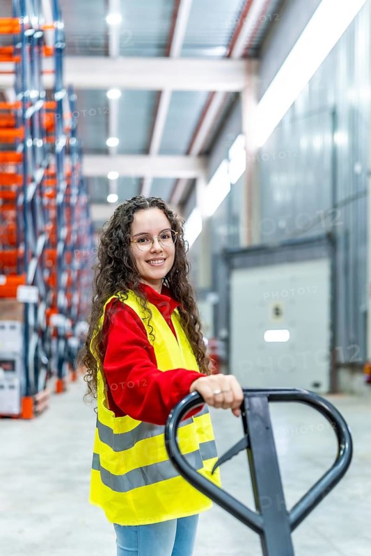 Vertical portrait of a happy young cauacsian woman working with low lift forklift in a distribution warehouse