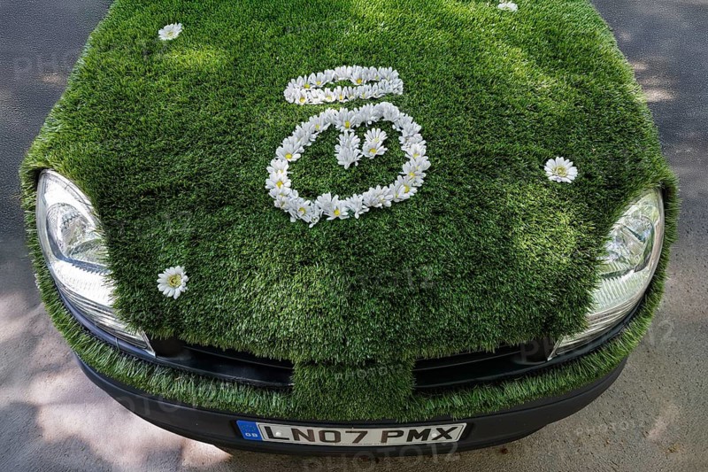 Bonnet of a small car covered with green artificial turf, face with halo of artificial daisies, campaign for clean cars, environmentally friendly drive system, Düsseldorf, North Rhine-Westphalia, Germany
