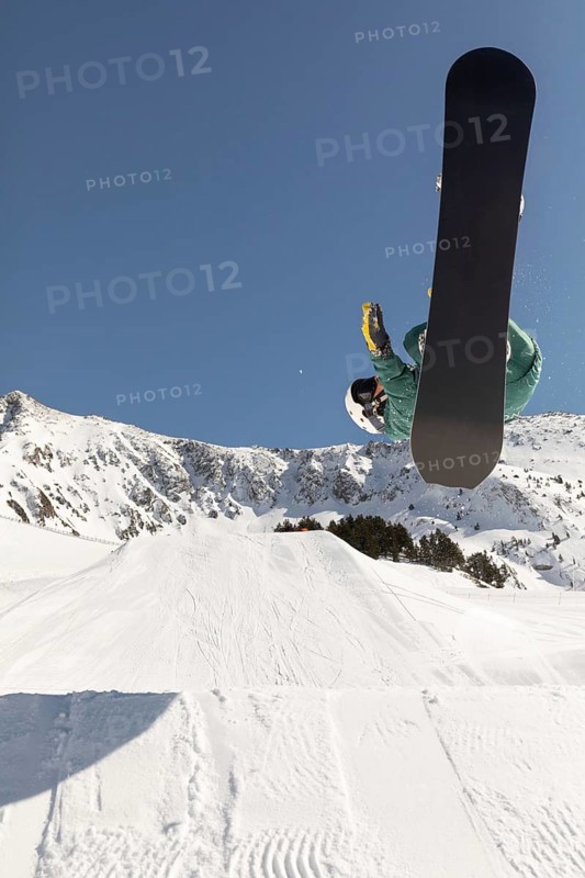 A snowboarder executes a thrilling aerial trick against a stunning mountainous backdrop, showcasing the excitement of freeriding in pristine powder snow under a clear blue sky