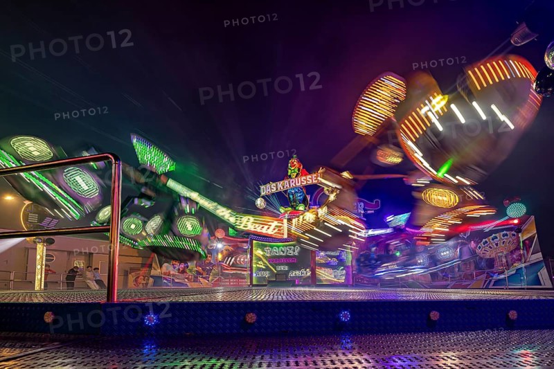 A carousel at a fair at night, surrounded by colorful light shows in fast motion, carousel and the hustle and bustle of summer winnings in Eisenach