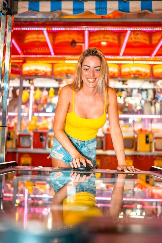 Vertical frontal photo of an adult caucasian woman playing air hockey on an amusement park at night