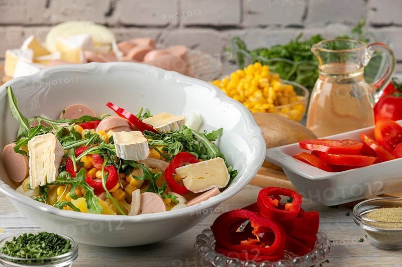 Potato salad with camembert, sausage and fresh arugula, surrounded by other ingredients