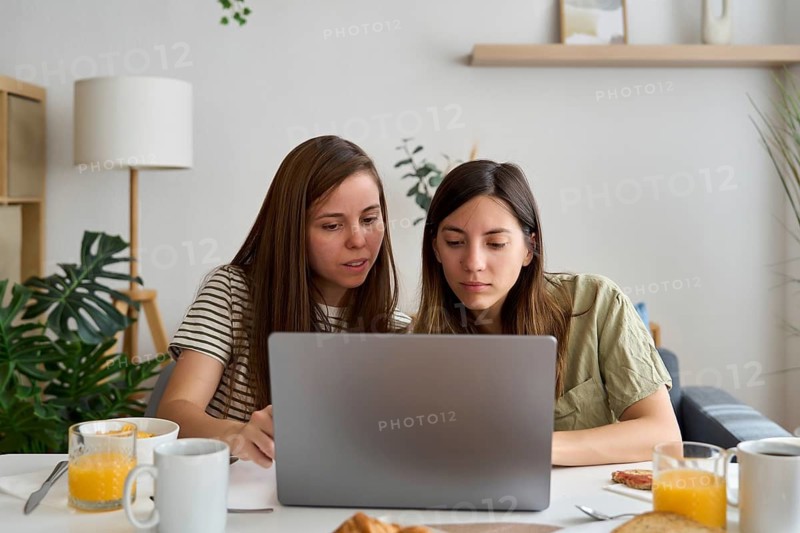 A lesbian couple sits closely together, focused on a laptop screen They appear engaged and collaborative, embodying teamwork and modern LGBTQIA+ representation