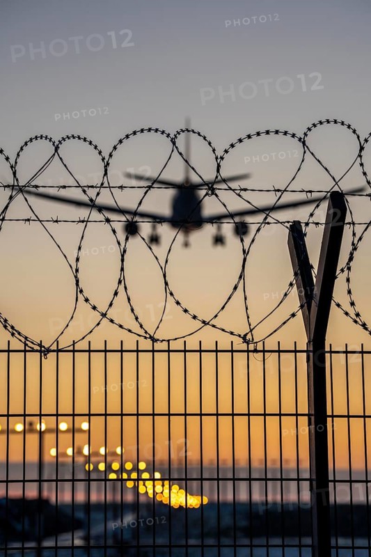 Symbolic image security at the airport, outer fence at Düsseldorf International Airport, steel wire fence, with S-wire rolls, NATO wire, on the top of the fence, aeroplane approaching, sunset, North Rhine-Westphalia, Germany