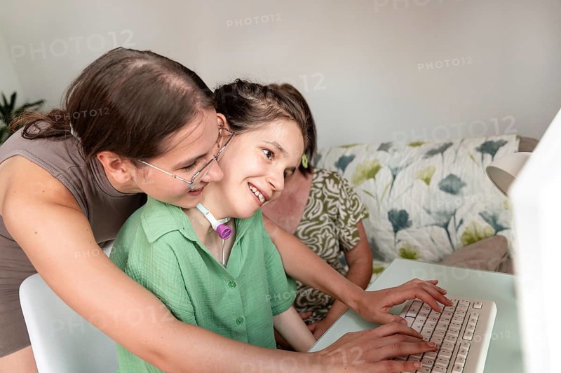 A loving family spends quality time with their disabled daughter, who has a tracheostomy, at home. The girl is engaged with a computer, smiling and surrounded by supportive family members